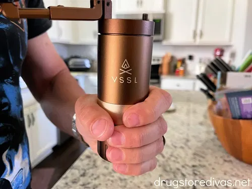 A man holding a gold VSSL coffee grinder in a home kitchen.