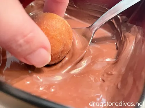 Fingers dipping a donut hole into melted chocolate.