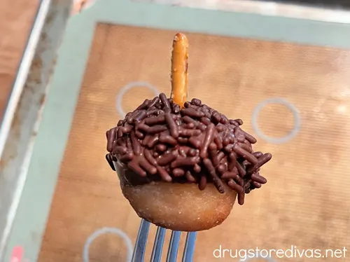 A donut hole on a fork with sprinkles on top and a pretzel stick sticking out.