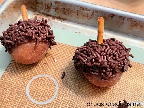 Two donut holes decorated to look like acorns on a silicone baking mat-lined cookie sheet.