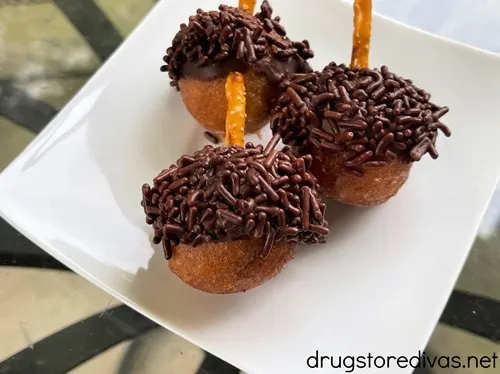 Three donut holes decorated to look like acorns on a white plate.