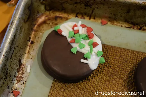 A black and white chocolate dipped Oreo cookie with Christmas sprinkles on top on a silicone baking mat.