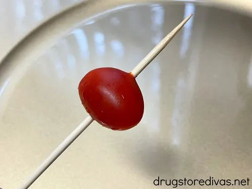 A grape tomato on a skewer over a gold plate.