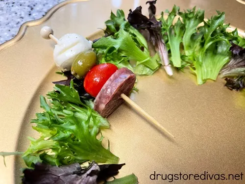 An antipasto skewer on top of green lettuce on a gold charger plate.