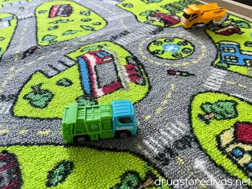 A playmat that's designed to look like a city with streets on it with a toy garbage truck and dump truck on top of it.
