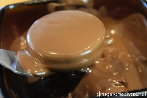 A dipped Oreo on a fork above a bowl of melted chocolate.