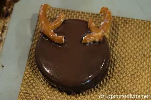A dipped Oreo cookie with pretzel antlers on a silicone baking mat.