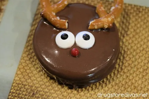 A dipped Oreo cookie with pretzel antlers, two candy eyes, and a red candy nose on a silicone baking mat.