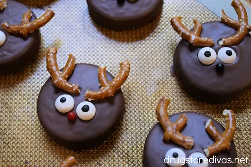 Five reindeer Oreo cookies on a silicone baking mat.