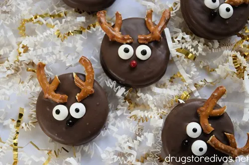 Five reindeer Oreo cookies on a baking tray with white and gold paper shred around them.