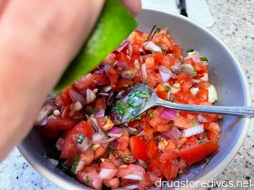 A hand squeezing half a lime over pico de gallo in a bowl.