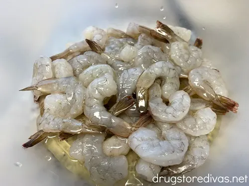 Frozen shrimp with tails on in a bowl with olive oil.