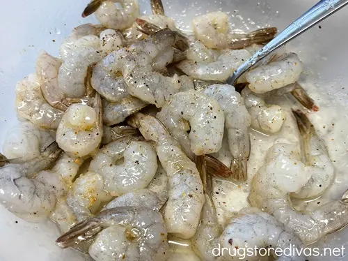 Frozen shrimp with tails on in a bowl with olive oil and seasoning.