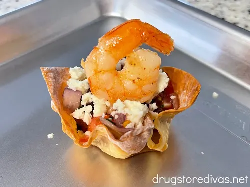 Pico de gallo, crumbled white cheese, and a shrimp with the tail up in a wonton cup on a silver tray.
