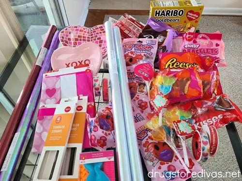 Various Valentine's Day candy, cellophane, plates, and tumbler straws on a table.