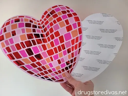 A hand holding two heart-shaped plates, one that looks like a pink disco ball and one that shows the white backside.