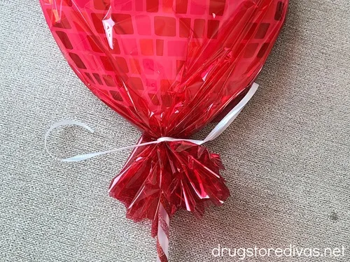 A heart-shaped lollipop in red cellophane that's gathered near the stick and tied with white curling ribbon.