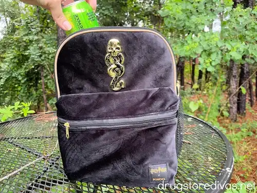A black Harry Potter-themed Igloo cooler backpack on a table with a hand pulling a green soda can out of it.