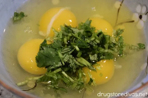 Four cracked eggs and chopped cilantro in a blue bowl.