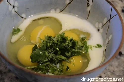 Milk, four cracked eggs, and chopped cilantro in a blue bowl.