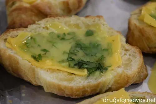 A raw egg and cilantro mixture on top of a slice of cheese that's on top of a cut open croissant on a silver tray.
