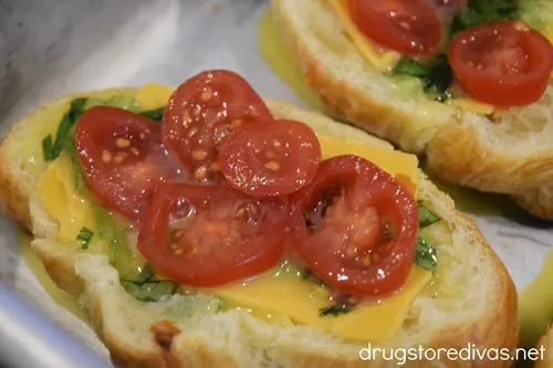 Sliced grape tomatoes, cheese, and herbs on top of a croissant that's cut open.