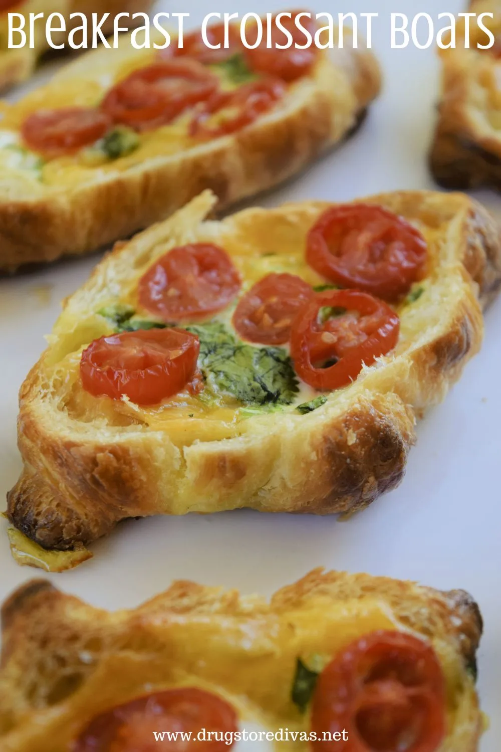 Five mini croissants with the tops cut off, filled with eggs, cilantro, and grape tomato slices on a white tray with the words 