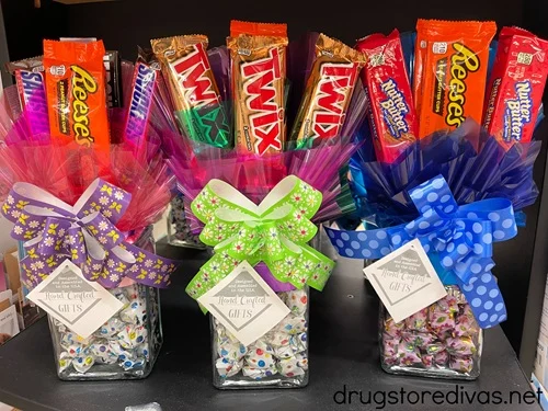 Three broquets: square, glass vases with candy in them and a bow on them with candy bars sticking out the top.