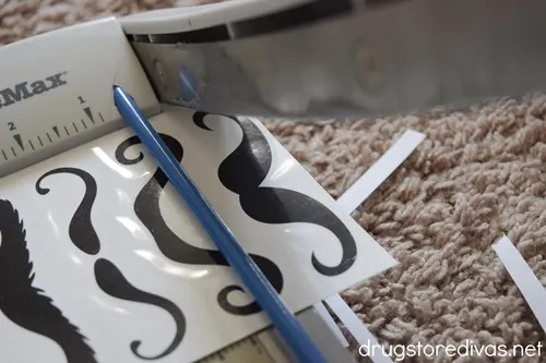 A paper trimmer cutting out tattoo mustaches.