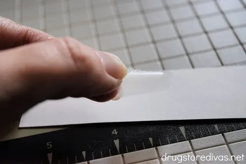 A hand holding a piece of tape that's about to be put on a white rectangular piece of paper.