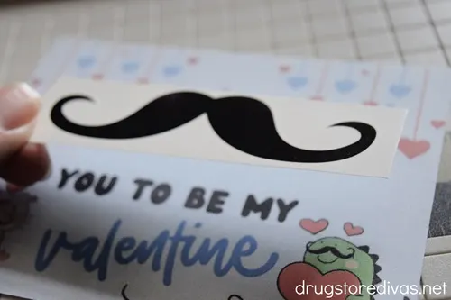 A mustache tattoo being held above a Valentine's Day card.