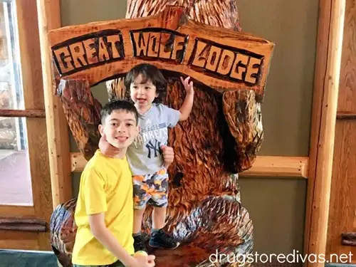 Two boys in front of a wooden bear statue that says Great Wolf Lodge.