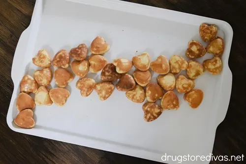 Mini heart-shaped pancakes going across a white serving tray.