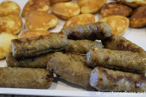 Breakfast sausage links and mini heart-shaped pancakes on a white serving tray.