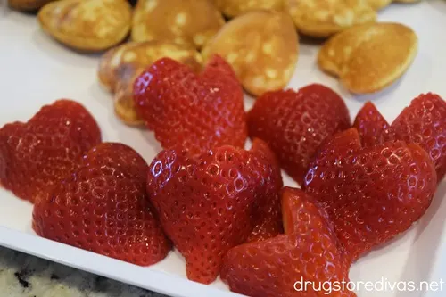 Heart-shaped strawberries and mini heart-shaped pancakes on a white serving tray.