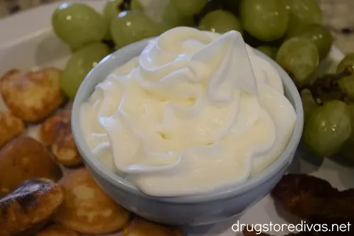 Whipped cream in a blue bowl with mini heart-shaped pancakes and green grapes around it on a white serving tray.