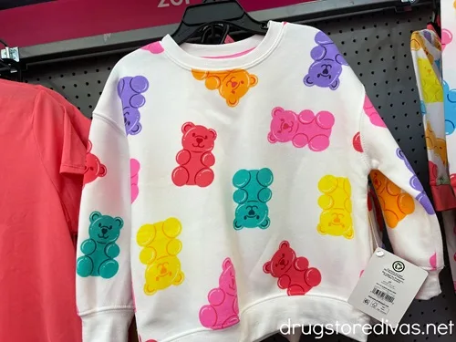 A white sweatshirt with colorful gummy bears on it hanging up in a store.