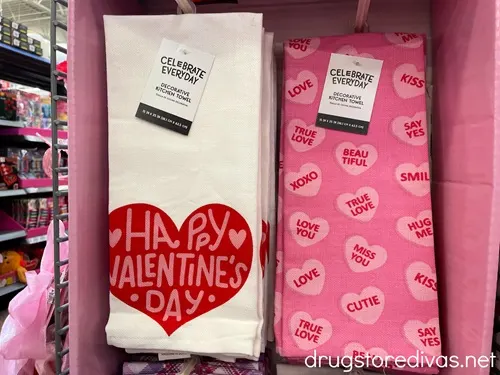Two Valentine's Day-themed kitchen towels hanging on a shelf in a store.