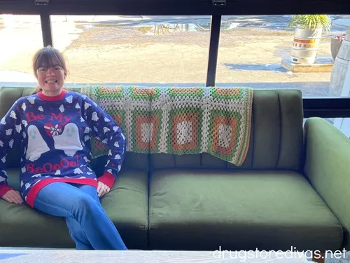 A woman in a Valloween sweater sitting on a green couch.