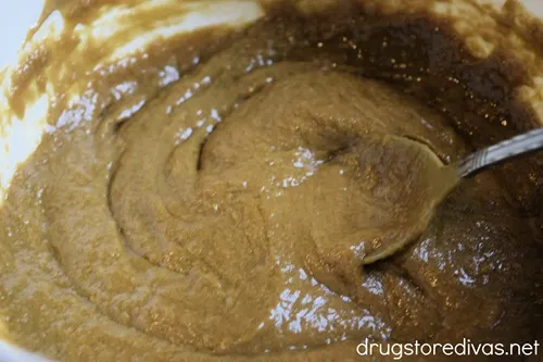 A brown cookie dough batter in a white bowl with a spoon.