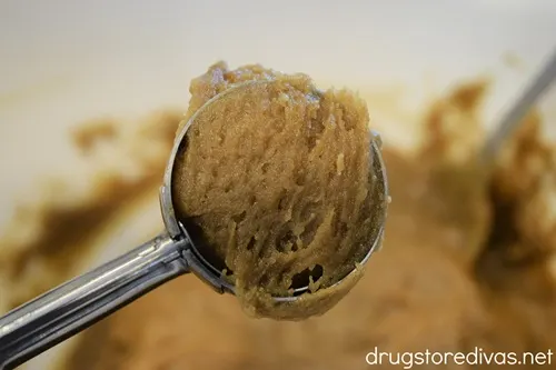A cookie scoop holding a brown cookie dough above a white bowl filled with the dough.