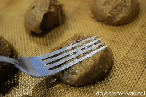A fork pressing down on a brown cookie dough ball with two cookie dough balls around it.