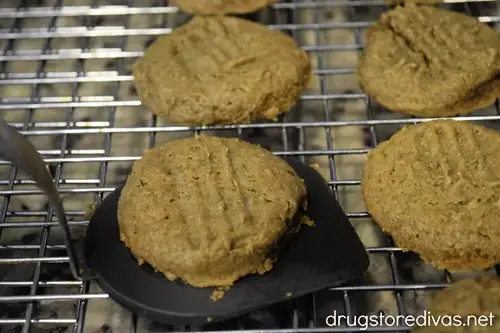 A brown cookie spatula holding a brown cookie about to put it on a wire rack where other cookies are.