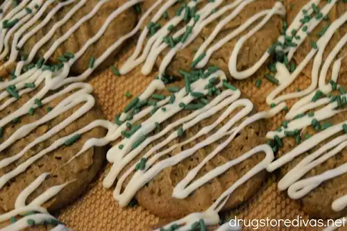 Six brown cookies with a white chocolate drizzle and green sprinkles on them.