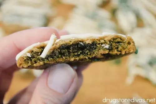 Two fingers holding half a brown cookie that has a green center that's pointing towards the camera.
