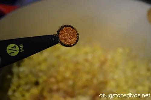 Tajin seasoning in a measuring spoon above a bowl that's filled with corn.