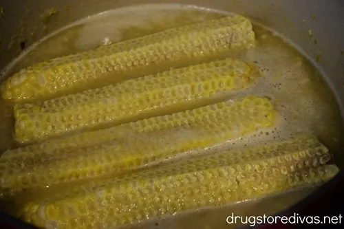 Four stripped corn on the cobs in a bowl with broth.
