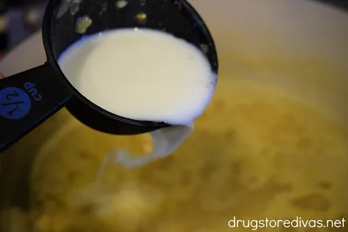 A measuring cup filled with milk being poured into a bowl that has broth in it.