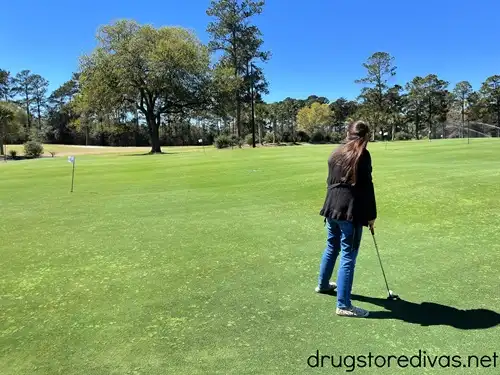 A woman in a long black jacket on a putting course.