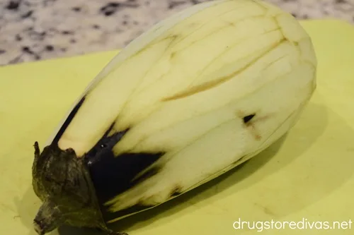 A peeled eggplant on a yellow green cutting board.